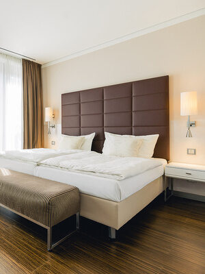 Helles Hotelzimmer mit Doppelbett, großen Fenstern und gemütlicher Sitzecke.