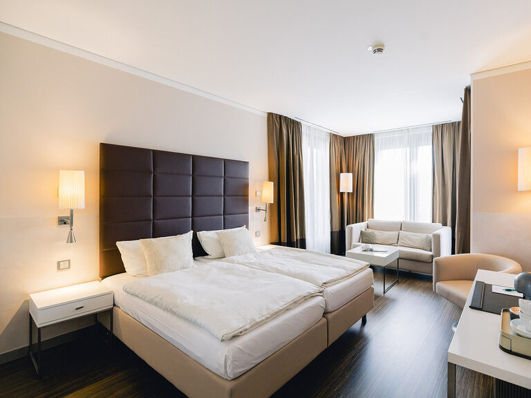 Modernes Doppelzimmer mit großem Bett, Stoffsofa, großen Fenstern und Schreibtisch