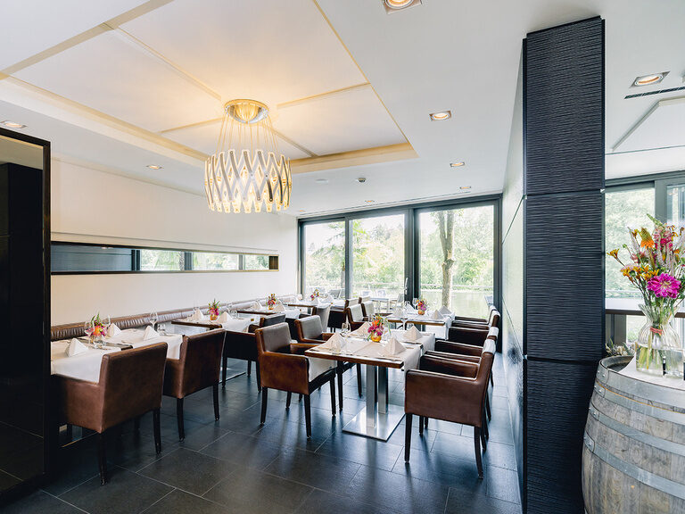 Modern eingerichteter Restaurantbereich mit gedeckten Tischen und großen Fensterfronten.